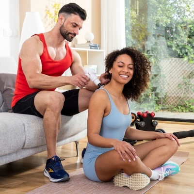 Homem a usar pistola de massagem no ombro de mulher sentada no chão