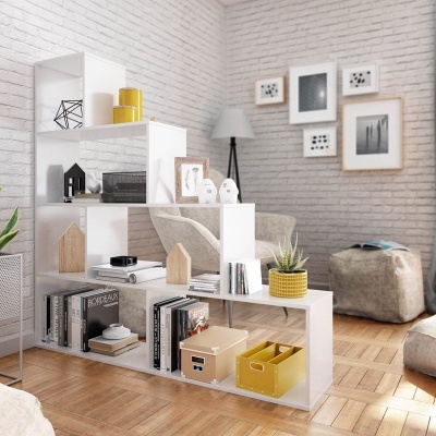 Estante branca multi-níveis com decoração e livros numa sala com parede branca de tijolo e pavimento em madeira