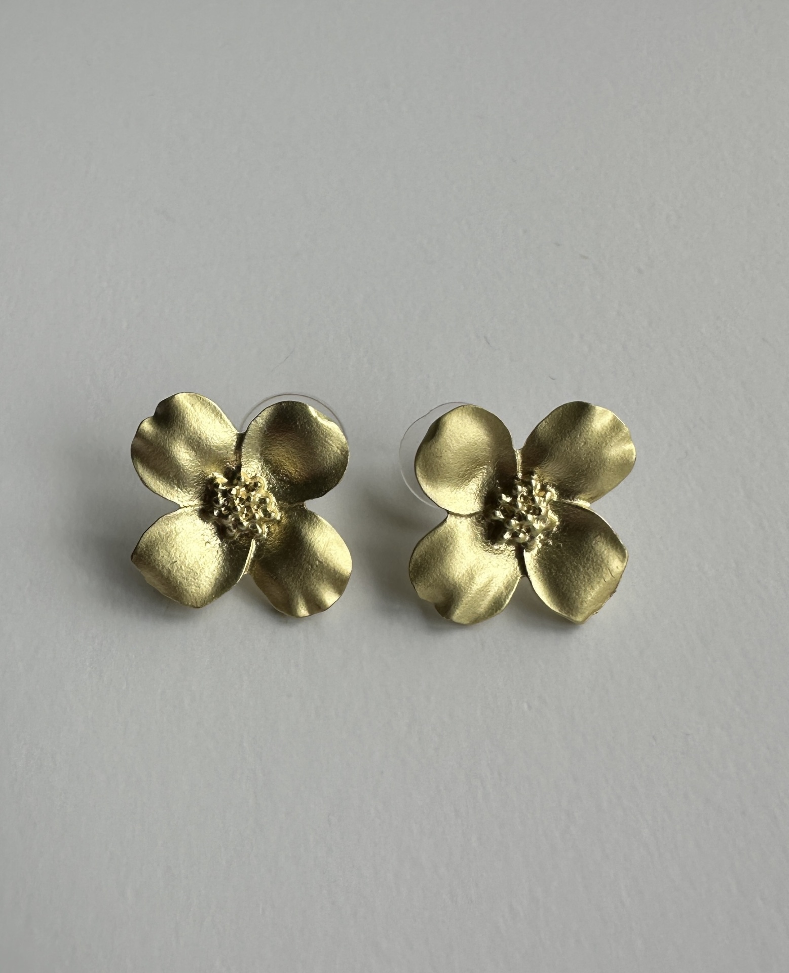 Brincos Flor Dourada "Radiância Eterna": O Seu Brilho, A Sua História Brincos dourados em forma de flor com quatro pétalas em fundo branco.