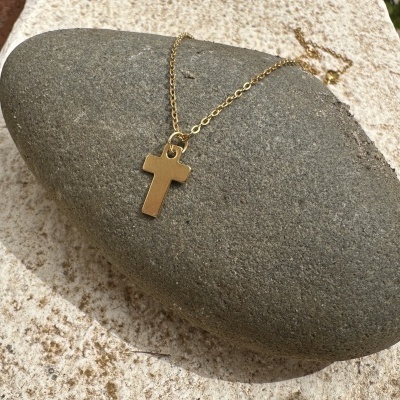 Colar dourado com pendente em forma de cruz sobre pedra cinzenta