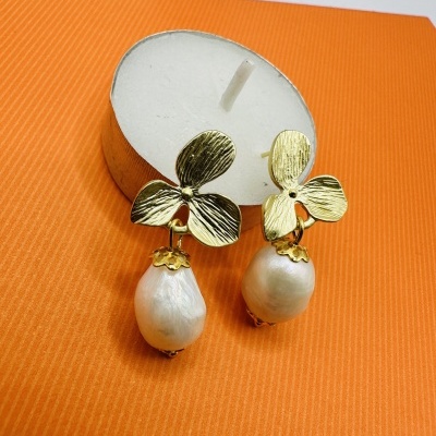 Brincos dourados com pérolas pendentes em fundo laranja