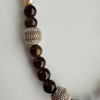 Colar ou pulseira com contas castanhas escuras, prateadas e amarelo-claro sobre fundo branco