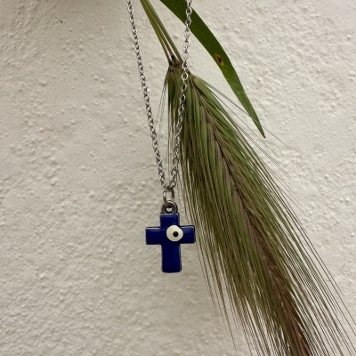 Colar com pendente em cruz azul e olho branco pendurado numa planta verde