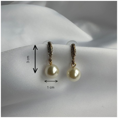 Brincos dourados com pérolas penduradas e detalhes brilhantes sobre tecido branco