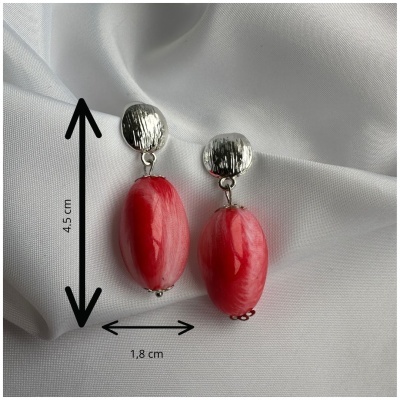 Brincos prateados com pendente oval vermelho sobre tecido branco.