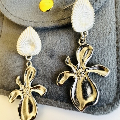 Brincos pendentes metálicos prateados com design de flor sobre suporte de tecido cinzento.