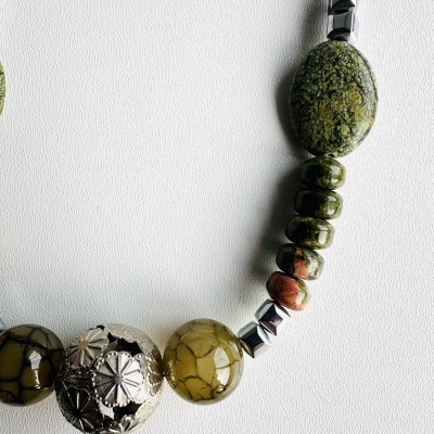 Colar com contas metálicas prateadas e pedras verdes texturizadas sobre fundo branco