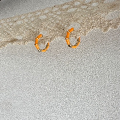 Brincos de argola laranja numa superfície texturada branca com padrão rendado bege na parte superior