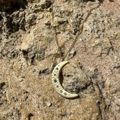 Colar com pendente em forma de lua crescente dourada sobre rocha arenosa