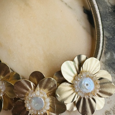 Colar de flores metálicas douradas com detalhes em pérola sobre mármore