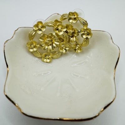 Prendedor dourado com flores em prato branco