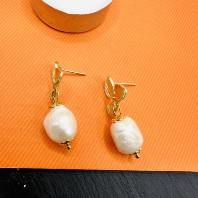 Brincos dourados com pérolas irregulares sobre fundo laranja