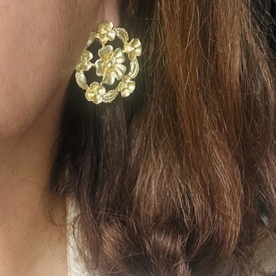 Brinco dourado em forma de círculo com flores e folhas, norelha esquerda