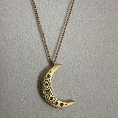 Colar de lua crescente dourada com pedras negras sobre fundo cinzento