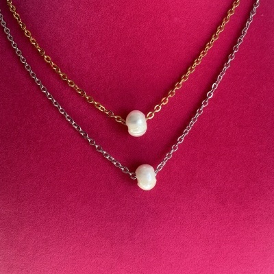 Dois colares, um dourado e um prateado, com pérolas brancas, sobre fundo vermelho