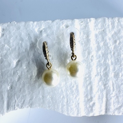 Brincos com pérolas brancas e base dourada sobre superfície branca texturada