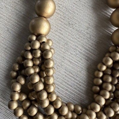 Colar de contas douradas com textura mate sobre superfície clara listrada.
