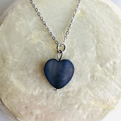 Colar com pendente coração azul escuro sobre superfície redonda clara