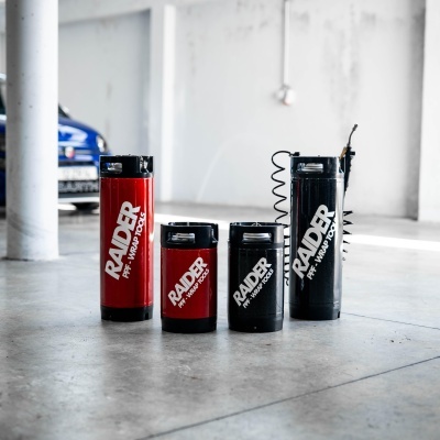 Compressores portáteis RAIDER vermelhos e pretos em chão de garagem com carro azul ao fundo