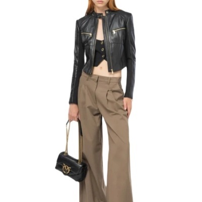 Modelo com casaco preto em pele, calças largas bege e mala preta com alça dourada