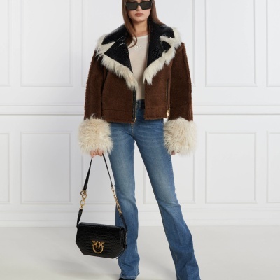 Mulher com casaco castanho felpudo com gola preta e pêlo branco, jeans azuis, t-shirt branca, a segurar mala preta com pormenores dourados.