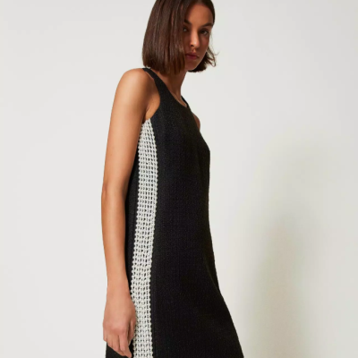 Vestido curto preto com faixa lateral branca, sem mangas, modelo com cabelo curto em fundo branco.