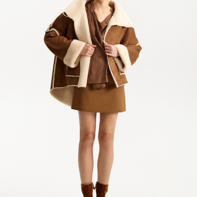 Mulher com casaco oversized castanho com interior de pele de ovelha e botins castanhos de veludo.
