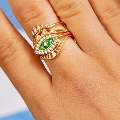 Anel dourado com pedra verde e cristais em formato de olho no dedo