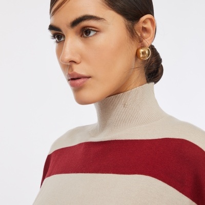 Mulher a usar camisola de gola alta com riscas vermelhas e bege e brinco dourado redondo