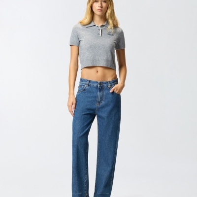 Mulher vestindo camisola cinza curta, jeans azuis largos e sapatos prateados em fundo branco