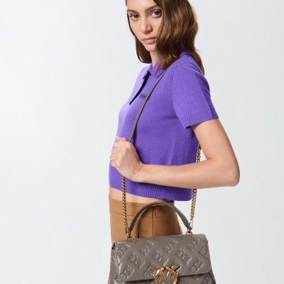 Mulher com camisola roxa e calças castanhas segurando mala cinza com padrão em relevo