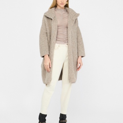 Mulher com casaco bege felpudo, blusa bege clara, calças creme e botas pretas com fivela dourada.