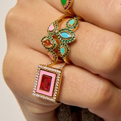 Anéis dourados com pedras coloridas e cristais em dedo segurando peça metálica