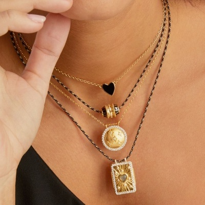 Colares dourados femininos em camadas com diferentes pingentes, em modelo com roupa preta.