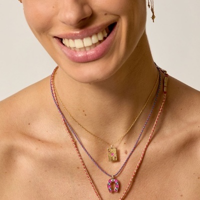 Colares e brincos dourados com pendentes coloridos usados por uma mulher sorridente