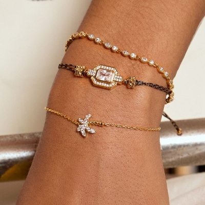 Três pulseiras douradas com pedras brilhantes no pulso de uma pessoa.