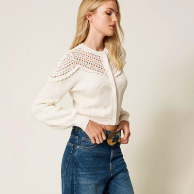 Mulher a usar camisola branca de malha com gola em crochê e calças de ganga azuis