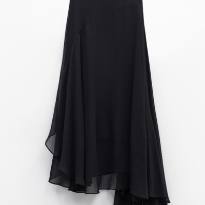 Saia preta assimétrica de tecido leve e transparente pendurada numa parede branca