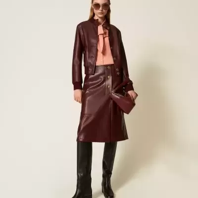 Conjunto feminino com jaqueta e saia de couro vinho, blusa rosa, botas pretas e bolsa vinho