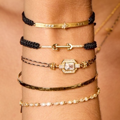 Conjunto de cinco pulseiras douradas e pretas com detalhes brilhantes no pulso