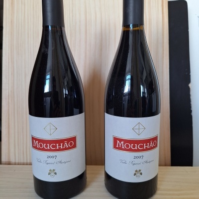 Duas garrafas de vinho tinto Mouchão de 2007 com rótulo branco e vermelho em superfície de madeira