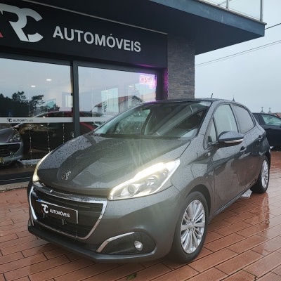 Carro cinzento estacionado à frente de loja RC AUTOMÓVEIS com faróis ligados