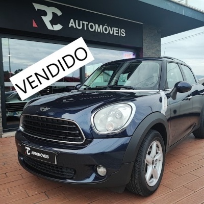 Mini Cooper azul escuro à frente de loja RC AUTOMÓVEIS com placa VENDIDO
