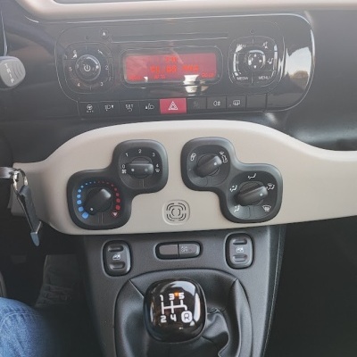 Painel central de carro com rádio, controles de ar condicionado e alavanca de câmbio manual.