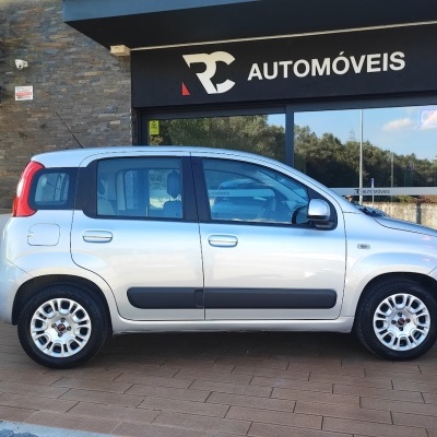 Carro cinza prateado de cinco portas estacionado em frente a loja RC Automóveis