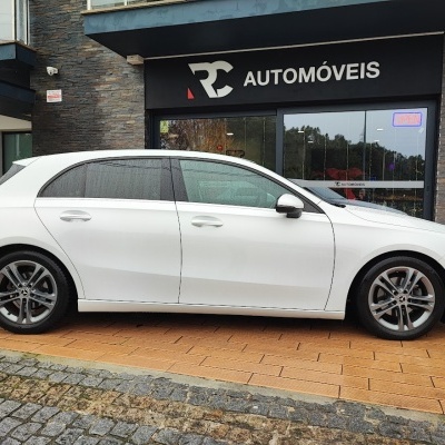 Carro branco de cinco portas estacionado em frente a loja RC AUTOMÓVEIS.