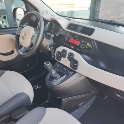 Interior de carro Fiat com volante bege e preto e painel central com rádio e comandos de ar condicionado