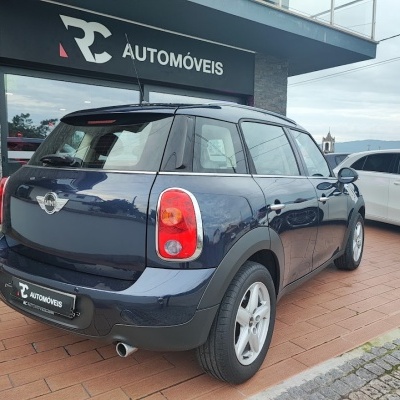 Carro MINI azul escuro em exposição frente a uma loja com placa RC AUTOMÓVEIS