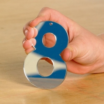 Número 8 metálico espelhado na mão de uma criança sobre mesa de madeira