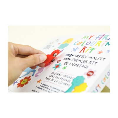 Caixa colorida com texto MY FIRST COLOUR KIT e mão segurando peça vermelha sorridente